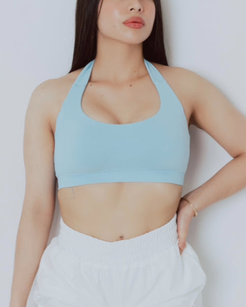 Woman wearing a light blue sports bra and white shorts on a plain background